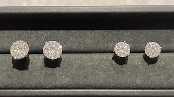 Cuatro aretes de diamantes de corte brillante colocados en dos pares sobre una ranura de terciopelo oscuro dentro de un estuche.
