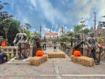 Dos estatuas de caballeros con armadura flanquean una reja metálica decorada con calabazas, fardos de paja y un cartel de Halloween
