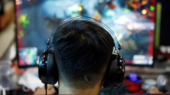 Vista trasera de la cabeza de una persona con cabello oscuro y auriculares negros, mirando una pantalla de computadora que muestra un juego en línea vibrante