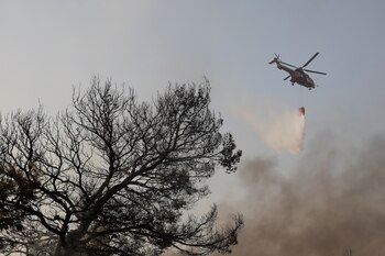 Un helicóptero de extinción de incendios hace una gota de agua mientras un incendio forestal arde en el suburbio de Varympompi al norte de Atenas, Grecia, el 4 de agosto de 2021. REUTERS / Costas Baltas