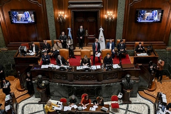 Vista superior de un recinto de madera con personas en sus escritorios, banderas, dos pantallas de televisión y bustos de bronce
