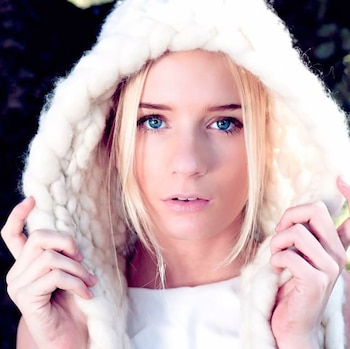 Delfina Lanusse sonríe a la cámara con la cabeza inclinada, apoyándose en un árbol en una calle urbana con edificios y autos estacionados