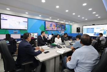 Personas sentadas a una mesa de conferencia en una oficina equipada con pantallas en la pared que muestran mapas e información