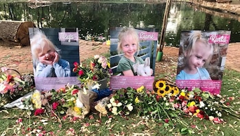 Tres retratos de niñas pequeñas, Maya, Liané y Karla, se exhiben en un memorial al aire libre con flores, pétalos y un cuerpo de agua al fondo