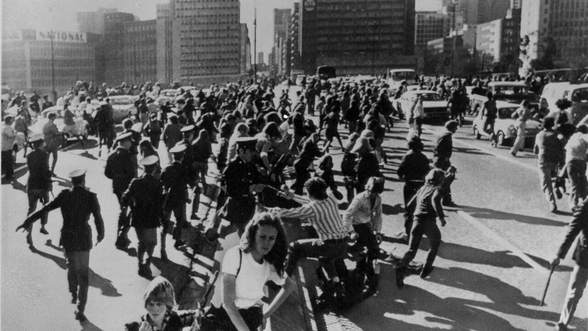 En oposición a las estrictas normas del apartheid de Sudáfrica, un grupo multirracial de estudiantes negros y blancos huye de la policía en Johannesburgo (AP)