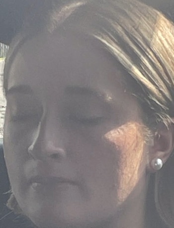 Primer plano del rostro de una mujer con los ojos cerrados y cabello castaño claro. Lleva un pendiente de perla en la oreja derecha. La luz del sol incide en su rostro