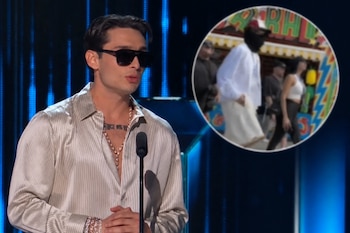 Hombre con gafas oscuras y camisa satinada frente a un micrófono, junto a un recuadro circular con dos figuras desenfocadas que caminan.