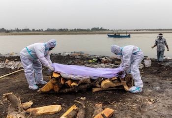 Hombres con trajes de protección colocan un paño blanco sobre el cuerpo de un familiar, fallecido por la enfermedad del coronavirus (COVID-19), antes de su cremación a orillas del río Ganges en Garhmukteshwar en el estado de Uttar Pradesh, India