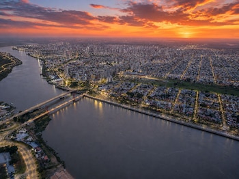 Fotografía aérea de una ciudad iluminada con puentes y edificios junto a un río bajo un cielo de atardecer