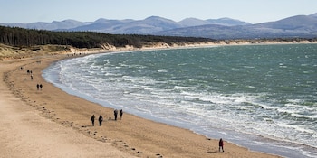 La playa de Llanddwyn destaca por su combinación de mar abierto, dunas naturales, bosque costero y una isla accesible a pie con la marea baja (Wikimedia Commons)