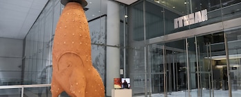 Escultura de terracota texturizada en un vestíbulo moderno con paredes de cristal. Hay una pantalla de video y el letrero 'ART CENTRAL HAUS' visible