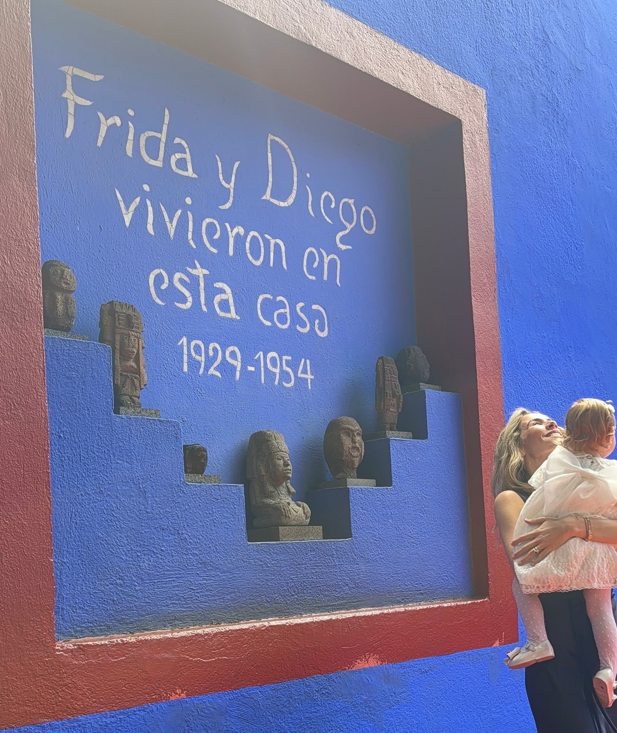 Elina Costantini sostiene a su hija Kahlo frente a una pared conmemorativa durante un recorrido por el Museo Frida Kahlo
