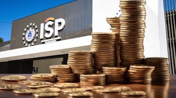 Edificio del Instituto Salvadoreño de Pensiones en segundo plano. Primer plano con pilas de monedas de dólar y monedas dispersas.