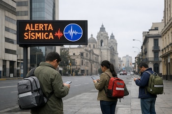 Un cartel digital muestra Alerta Sísmica con el logo del IGP. Tres personas de espaldas consultan sus teléfonos en una calle con edificios y vehículos.