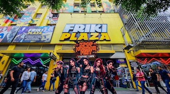 Fachada amarilla de Friki Plaza con un cartel del Kpop Horror Fest y varias figuras vestidas con ropa oscura en primer plano.