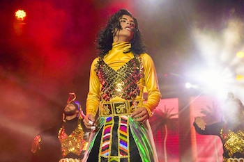 Gabriela Villanueva como Michael Jackson, mirando hacia arriba, con un traje amarillo brillante y adornos dorados, en un escenario iluminado con luces rojas