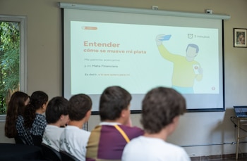 Un grupo de personas sentadas de espaldas observa una pantalla de proyección que exhibe una diapositiva sobre finanzas