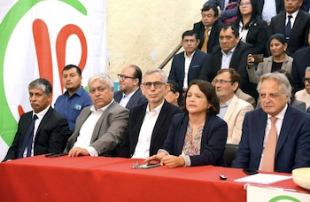 Un grupo de políticos y especialistas sentados en fila frente a una mesa roja, con un logotipo grande de "JPP" parcialmente visible al fondo, en un evento