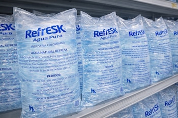 Múltiples bolsas de plástico transparente con agua de la marca Refresk Agua Pura y texto informativo, dispuestas en varias filas sobre un estante.