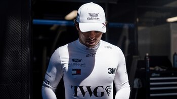 Un hombre con gorra y camiseta blancas con logotipos de patrocinadores y de Cadillac Formula 1 Team dentro de un garaje.