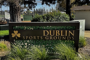 Letrero de madera con la inscripción Dublin Sports Grounds y un trébol, ubicado frente a un campo de juego cercado