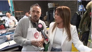 Un hombre con delantal de cocina blanco habla frente a un micrófono que sostiene una mujer vestida con una chaqueta blanca