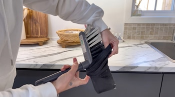 Unas manos sujetan un cepillo de limpieza gris y le colocan un calcetín negro sobre las cerdas en una encimera de cocina.