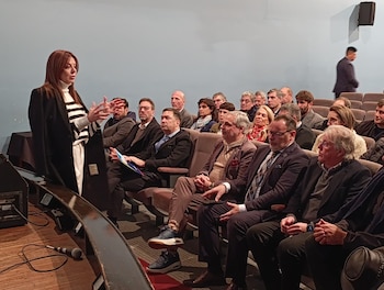 Sandra Pettovello y una comitiva caminan por un amplio salón con piso de baldosas, ventanas altas y sillas alineadas a los lados