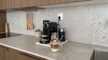Encimera de cocina con una cafetera de cápsulas, un espumador, un frasco con cápsulas, un vaso de café con leche y utensilios de madera.