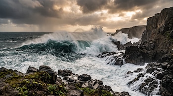 Olas del mar rompen contra acantilados rocosos bajo un cielo cubierto de nubes