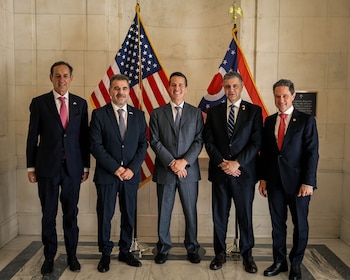 Cinco hombres en traje posan alineados frente a las banderas de Estados Unidos y del estado de Ohio en el interior de un edificio