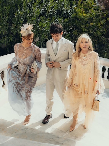 Tres personas descienden una escalera de mármol al aire libre. Charles Leclerc viste un traje beige, flanqueado por dos mujeres con vestidos de gala