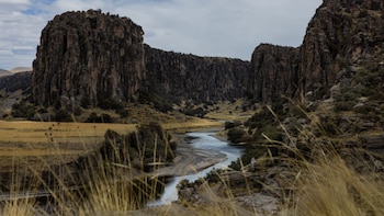 Un cañón con paredes rocosas y un río en el fondo bajo un cielo parcialmente nublado