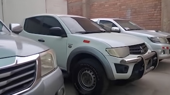 Tres camionetas pickup blancas estacionadas en fila, con la parte frontal de una en primer plano. Detrás, una pared de ladrillos
