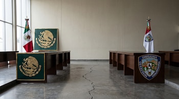 Salón con mesas y símbolos de México y Chihuahua enfrentados. Una grieta en el suelo, entre ambos lados, sugiere una clara separación.