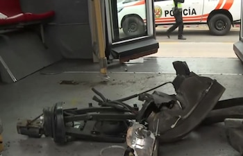 Interior de un bus del Metropolitano con partes metálicas y cables rotos esparcidos en el suelo; se ve un vehículo policial blanco y un agente afuera