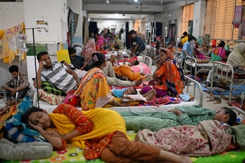 Varias personas y niños descansan sobre camas metálicas alineadas en la sala de un hospital