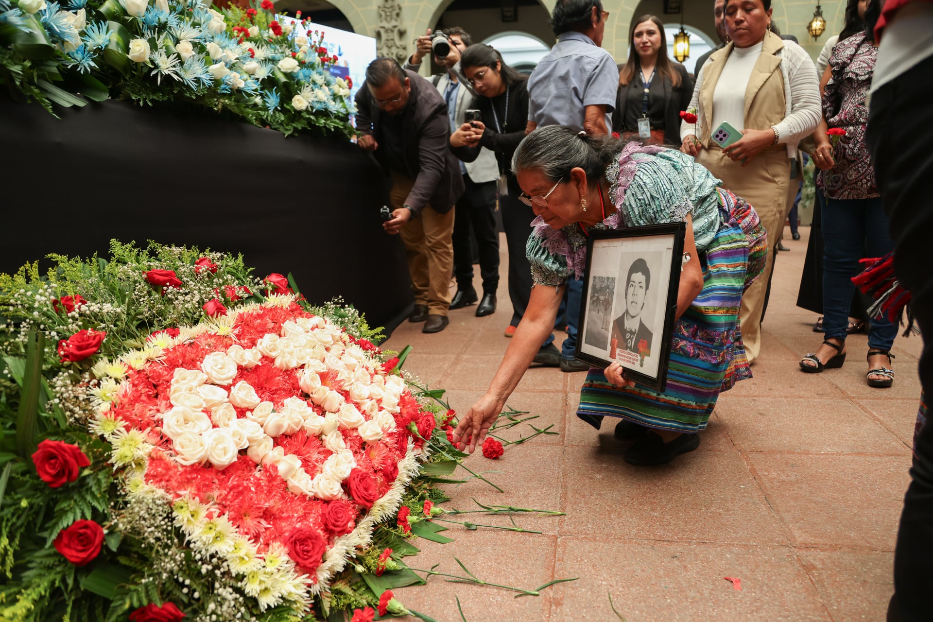 FOTODELDÍA AME2449. CIUDAD DE GUATEMALA (GUATEMALA), 19/06/2026.- Una familiar de desaparecidos pone una flor en un altar durante un acto conmemorativo este viernes, en Ciudad de Guatemala (Guatemala). En el marco del día Nacional contra la Desaparición Forzada en Guatemala, que se conmemora cada 21 de junio, se realizó el lanzamiento del mecanismo de búsqueda humanitaria de personas desaparecidas durante el conflicto armado interno en Guatemala 2026-2036, en el Palacio Nacional de la Cultura en Ciudad de Guatemala. EFE/ Mariano Macz