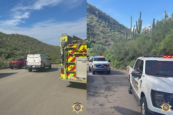 Dos camionetas de la Oficina del Sheriff con luces de emergencia, un camión de bomberos y una camioneta roja en una carretera entre montañas con cactus saguaro