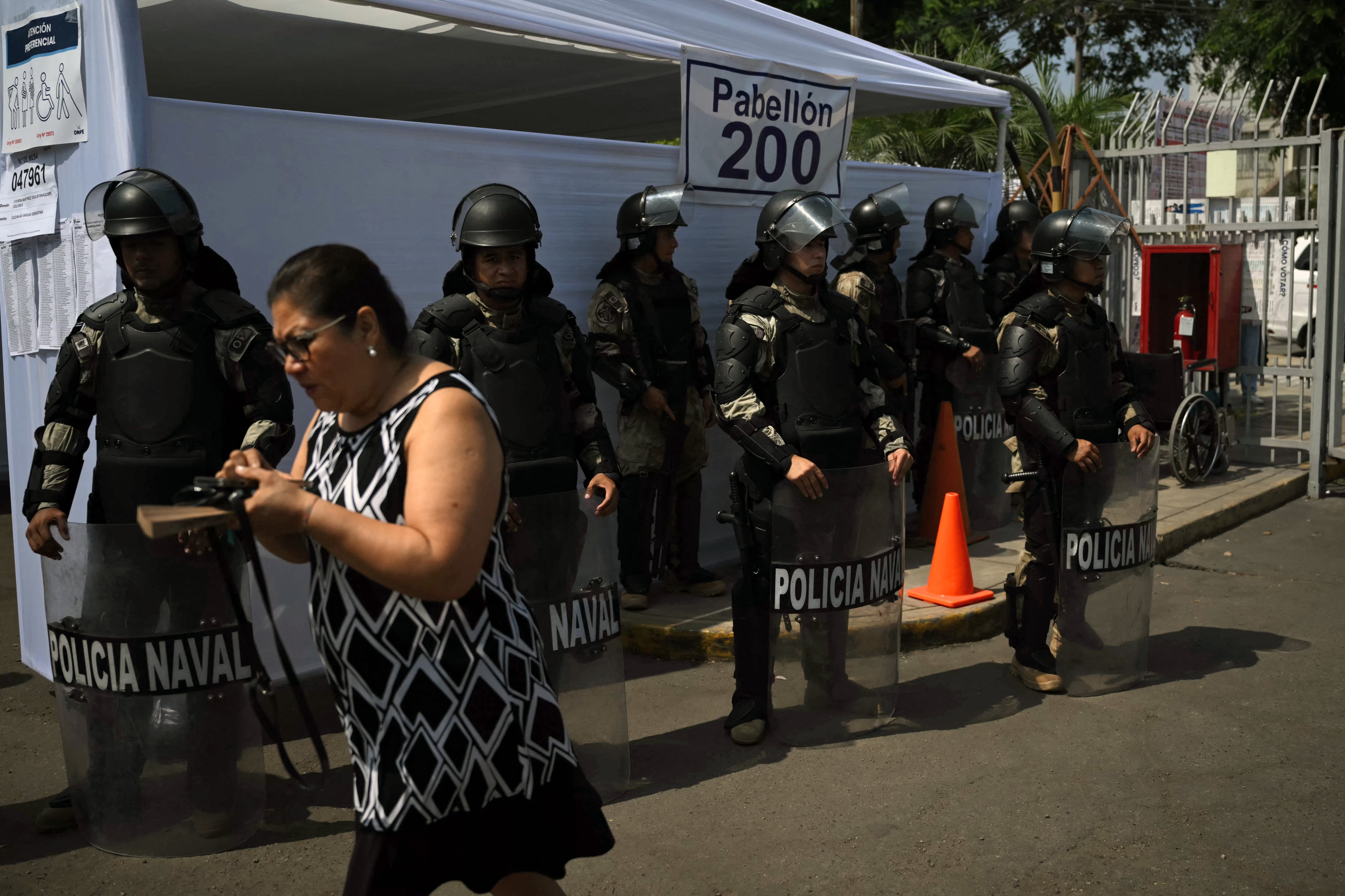 A woman walks past police members standing guard outside a polling station during the presidential election in Lima on April 12, 2026. Peruvians head to the polls to elect its ninth president in a decade, from a record field of 35 candidates, with crime-weary voters seemingly poised to extend the tide of conservative governments sweeping Latin America. (Photo by Luis ROBAYO / AFP)