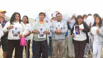 Un grupo de personas en una playa de arena sostiene fotografías impresas de un joven y globos blancos