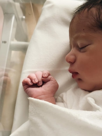 Primer plano de un bebé recién nacido durmiendo de lado en una cuna, cubierto con una manta blanca, con su pequeña mano en puño visible
