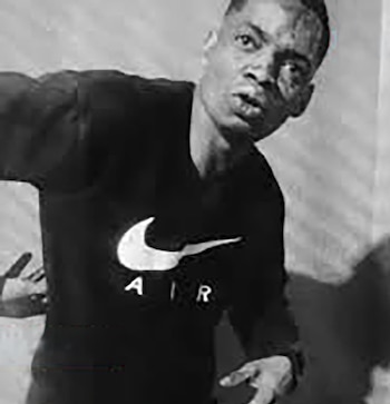 Primer plano en blanco y negro de un hombre de piel oscura con cabello corto, mirando al frente, vestido con una camiseta negra con el logo blanco de 'Nike Air'