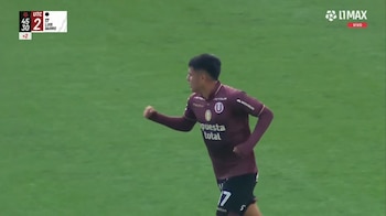 Un futbolista con la camiseta granate de Universitario corre con el puño cerrado sobre un campo de césped verde
