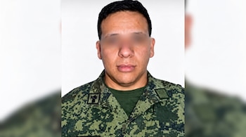 Retrato frontal de un hombre con uniforme militar pixelado verde y los ojos cubiertos por un difuminado sobre un fondo blanco.