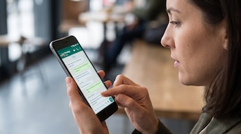 Perfil de una mujer sosteniendo un teléfono inteligente que muestra una interfaz de conversación de WhatsApp.