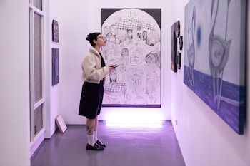 Una mujer de pie en un espacio con luz violeta mira cuadros y una ilustración de gran tamaño colgados en las paredes