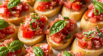 Primer plano de varias rebanadas de pan tostado con trozos de tomate rojo, hojas verdes de albahaca y queso blanco rallado.