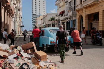 Vecinos ayudan a mover un coche averiado en una calle habanera marcada por la acumulación de residuos y el deterioro urbano