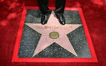 Primer plano de los pies de un hombre con zapatos negros sobre la estrella de Paulinho da Costa en el Paseo de la Fama de Hollywood, sobre una alfombra roja